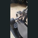 Detailní pohled na kový mechanismus basového pedálu s černou základnou a šedým stupňem. Konstrukce je z chromovaného kovu s viditelnými šrouby a nast…
