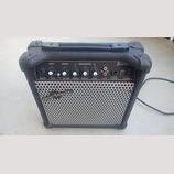 Černý kytarový kombozesilovač v plastovém kufru s rukojetí. Na horním ovládacím panelu jsou nápisy DRIVE, MASTER, EQUALIZATION, GUITAR AMP, INPUT, GA…
