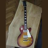 Elektrická kytara typu Les Paul s barevným přechodem od žluté přes červenou k hnědé. Na hlavě hmatníku je nápis Luxury a na krku u první pražnice ozn…