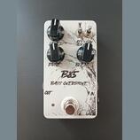 Bílý efekt pedál s nápisy B85 a BASS OVERDRIVE. Obsahuje tři černé otočné knoflíky s popisky LEVEL, DRIVE a BLEND, dva přepínače s nápisy ATTACK a GR…