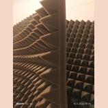 Fotografie zobrazuje šedé akustické pěnové panely s pyramidovitou strukturou. Panely jsou umístěny vedle sebe, jeden z nich je natočen z profilu. Pov…