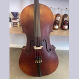 Hnědý smyčcový nástroj, pravděpodobně violoncello, s viditelnou strukturou dřeva a opotřebováním laku na hranách. Nástroj má čtyři struny, bílý kobyl…