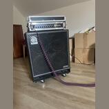 Černý basový kombozesilovač s mřížkou z kovového pletiva a nápisy Ampeg v horní části a PRO NEO v pravém dolním rohu. Na horní hraně boxu je umístěn…
