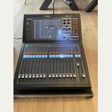 Černý digitální mixovací pult značky YAMAHA, model QL1. Horní část obsahuje barevný displej s ovládacími prvky, několik posuvníků a tlačítek. Spodní…
