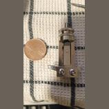 Fotografie zachycuje kovový hudební komponent, pravděpodobně součástku k ladění nebo mechaniku. Na boku je svisle vyražen nápis SWITCHCRAFT. Součástk…