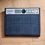 Černý elektronický bicí pad značky ALESIS, model PERFORMANCE PAD PRO. Zařízení obsahuje mřížku z gumových políček a ovládací panel s displejem, tlačí…