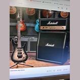 Fotografie zachycuje elektrickou kytaru s černým gradientem a dvě komba značky Marshall. Horní kombo má nápis Marshall a modelové označení JVM, spodn…