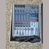 Stříbrný mixážní pult Behringer X2042USB umístěný v otevřeném transportním kufru. Na horní části jsou vidět konektory pro mikrofony, linkové vstupy a…