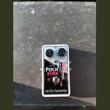 Kytarový efekt pedál v bílém kovovém krytu s černým ovládacím panelem. Na pedálu jsou nápisy PITCH FORK a electro-harmonix, dva černé otočné knoflíky…