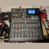 Digitální mixážní pult černé barvy s nápisem X32 PRODUCER a logem Behringer. Zařízení obsahuje displej, zahlreiche posuvníky, tlačítka a otočné ovlad…