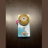 Kytarový efekt pedál v bílo-modrém provedení s grafickým motivem. Na horní části je umístěno žluté kolečko s nápisy TONE WHEEL, BY SALVATION AUDIO a…