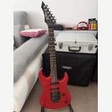 Červená elektrická kytara s černým hmatníkem a černou hlavou. Na hlavě je bílý nápis "Jet Rock". Kytara má dva snímače, ovládací knoflíky a je umístě…