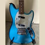 Modře metallic elektrická kytara s bílo-perleťovým pickguardem a hnědým hmatníkem. Na kovovém mostě je vyryto "MADE IN JAPAN" a "Fender". Povrch laku…