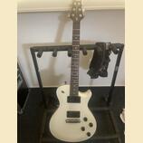 Bílá elektrická kytara s tmavým hmatníkem umístěná na černém stojanu. Na hlavě kytary je nápis "PRS Tremonti". Tělo má dva humbuckery, tři ovládací k…