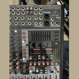 Detailní pohled na míchací pult stříbrné barvy s černými ovládacími prvky. V horní části je nápis EURODESK SX2442FX, ULTRA-LOW NOISE DESIGN 24-INPUT…