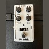 Bílý efekt pedál s nápisy RACER a MH pedals. Obsahuje čtyři černé ovládací knoflíky s popisky GAIN, TREBLE, VOLUME a BASS, vstup INPUT, výstup OUTPUT…