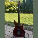 Elektrická kytara s červeným lesklým povrchem korpusu a hnědým hnedým hmatníkem. Na hlavě je bílý nápis Ibanez. Nástroj má dva humbuckery, kobylku s…