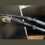 Detailní pohled na dva černé audio kabely s konektory. Jeden z nich má stříbrný kovový konektor a druhý je celý v černé barvě. Povrchy kabelů a konek…