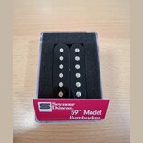 Dvě černé humbuckery s viditelnými bílými póly, umístěné v průhledném plastovém boxu s černou pěnovou vložkou. Na růžovém papírovém pásku je uveden n…