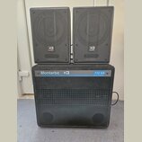 Sada tří černých reproduktorů, která obsahuje dva menší horní reproduktory a jeden velký spodní subwoofer. Na všech třech je viditelné logo s nápisem…