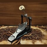 Černý basový pedál s kovovým šlapadlem a stříbrnými detaily. Pedál je vybaven bílým plstěným beaterem na kovovém rameni. Povrch šlapadla vykazuje mír…