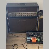 Černý kytarový zesilovač s nápisem Framus a označením modelu Dragon. Pod ním stojí hnědý kytarový box se stejným logem Framus. V popředí je černý ped…