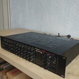 Černý 12kanálový mixážní pult s nápisy Roland M-12E a 12CHANNEL MIXER. Horní kryt obsahuje schéma s názvem M-12E BLOCK DIAGRAM. Zařízení vykazuje mír…