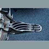Detailní pohled na kový pedál basového bubnu v černé a stříbrné barvě. Na stupni je viditelný oválný nápis Gibraltar. Povrch pedálu vykazuje známky b…