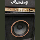 Detail kytarového komba značky Marshall. Horní část tvoří zlatý ovládací panel s nápisem JCM 800 LEAD SERIES a řadou otočných knoflíků. Spodní část u…