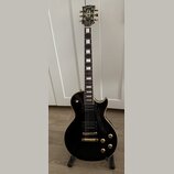 Černá elektrická kytara typu Les Paul se zlatými hardwaremi a bílými blokovými vložkami na hmatníku. Na hlavě je nápis Orville a pod ním menší text b…