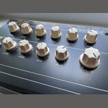 Černý elektronický přístroj s řadou bílých plastových oválových ovladačů. Na horní hraně jsou nápisy 12 VDC, OVERALL, GATE, SWITCH, AUDIO, MIDI IN, M…