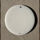 Bílá kruhová bubenová koží v kovovém obruči. V horní části je černé logo „dw drums“ a nápis „coat batter“. Dole se nachází modré logo „Remo“ a text „…