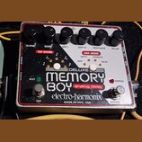 Efekt pedál analogového delay s bílo-černým povrchem a červeným rámem. Na zařízení jsou nápisy DELUXE MEMORY BOY analog delay, electro-harmonix a MAD…