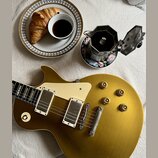 Zlatá elektrická kytara s tvarem singlecut, krémovým pickguardem a dvěma humbuckery. Na kytaru jsou vidět drobné škrábance a opotřebení povrchu. Vedl…