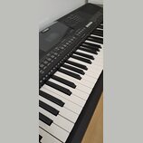 Černý digitální klavír s bílými a černými klávesami. V levé horní části je viditelné logo YAMAHA. Ovládací panel obsahuje řadu tlačítek s nápisy jako…