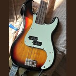 Elektrická basová kytara s korpusem v barevném přechodu od černého přes červený k žlutému. Nástroj má světle zelený pickguard a hnedý hmatník s kovov…
