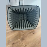 Šedý akustický odrazový štít s vnitřním povrchem z pyramidového akustického pěnového materiálu. Štít má obdélníkový tvar se zaoblenými rohy a černý t…