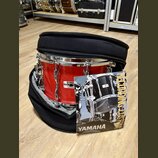 Červený buben v černém polstrovaném obalu. Na koruse je vidět štítek se značkou YAMAHA a nápisem MODEL: MADE IN JAPAN. Před nástrojem leží produktový…