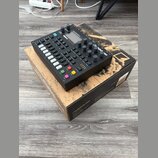 Černý digitální sekvencer a syntetizátor s nápisem Digitone, umístěný na originální krabici s nápisy Digitone a FM digital drum machine. Zařízení má…