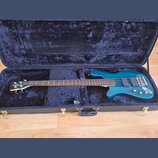 Modrá elektrická basová kytara v černém plišovém kufru. Na hlavě nástroje je bílý nápis RockBass. Tělo má dva snímače, tři ovládací knoflíky a kovový…