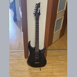 Černá elektrická kytara s prořezaným povrchem těla a hnedý hmatníkem. Na hlavě je bílý nápis Ibanez. Nástroj má dva humbuckery, jeden ovládací knoflí…