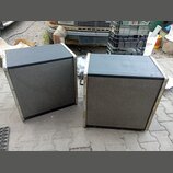 Dva černé reproduktorové boxy s šedou textilní maskou a světlými hranami. Povrch horníchdesek je černý, boční lišty vykazují známky opotřebení a koro…