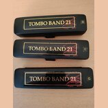 Tři černé harmoniky s nápisem TOMBO BAND 21 v zlatém rámečku. Každý nástroj má v pravém horním rohu označení tóniny: D, C a G. Na tělech jsou vidět n…