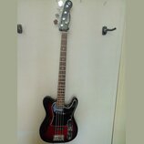 Čtyřstrunná basová kytara s černým korpusem v červeném sunburst provedení a bílým pickguardem. Na hlavě je svisle napsaný nápis RIS BASS. Nástroj má…