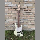 Bílá elektrická basová kytara s tmavým hmatníkem a bílým pickguardem. Na hlavě nástroje je viditelné logo "Squier". Kytara má čtyři struny a stříbrný…