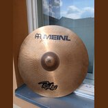 Kovový činel zlatavé barvy s viditelným kování povrchu. V horní části je modrý nápis MEINL s logem a pod ním menší text HAND MADE. V dolní části je č…