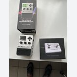 Na fotografii je stříbrný pedál s nápisy BEATBUDDY a SINGULAR SOUND, vybavený dvěma voliči Volume a Drum Set, displejem a tlačítkem TAP. Vedle něj je…
