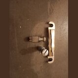 Fotografie zobrazuje tři kovové součástky ladicího mechanismu v chromovaném povrchu. Jsou vidět dvě ozubená kolečka a jedna kovová konzola s výřezy n…