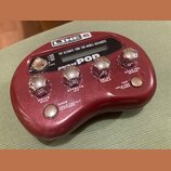 Vínový efektový procesor s nápisy LINE 6 a pocket POP. Zařízení má pět chromovaných otočných ovladačů s popisky DRIVE BASS, EFFECTS MID, DELAY TREBLE…