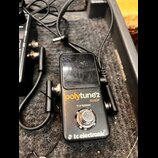Černý kytarový tuner v kovovém krytu s nápisy polytune 2 noir, true bypass a tc electronic. Povrch zařízení je viditelně poškrábaný a opotřebovaný. K…